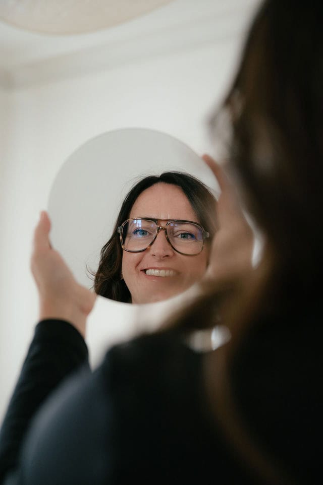 Daniela Reisner blickt in einen runden Spiegel, dabei sind man sie selbst und ihr Spiegelbild.