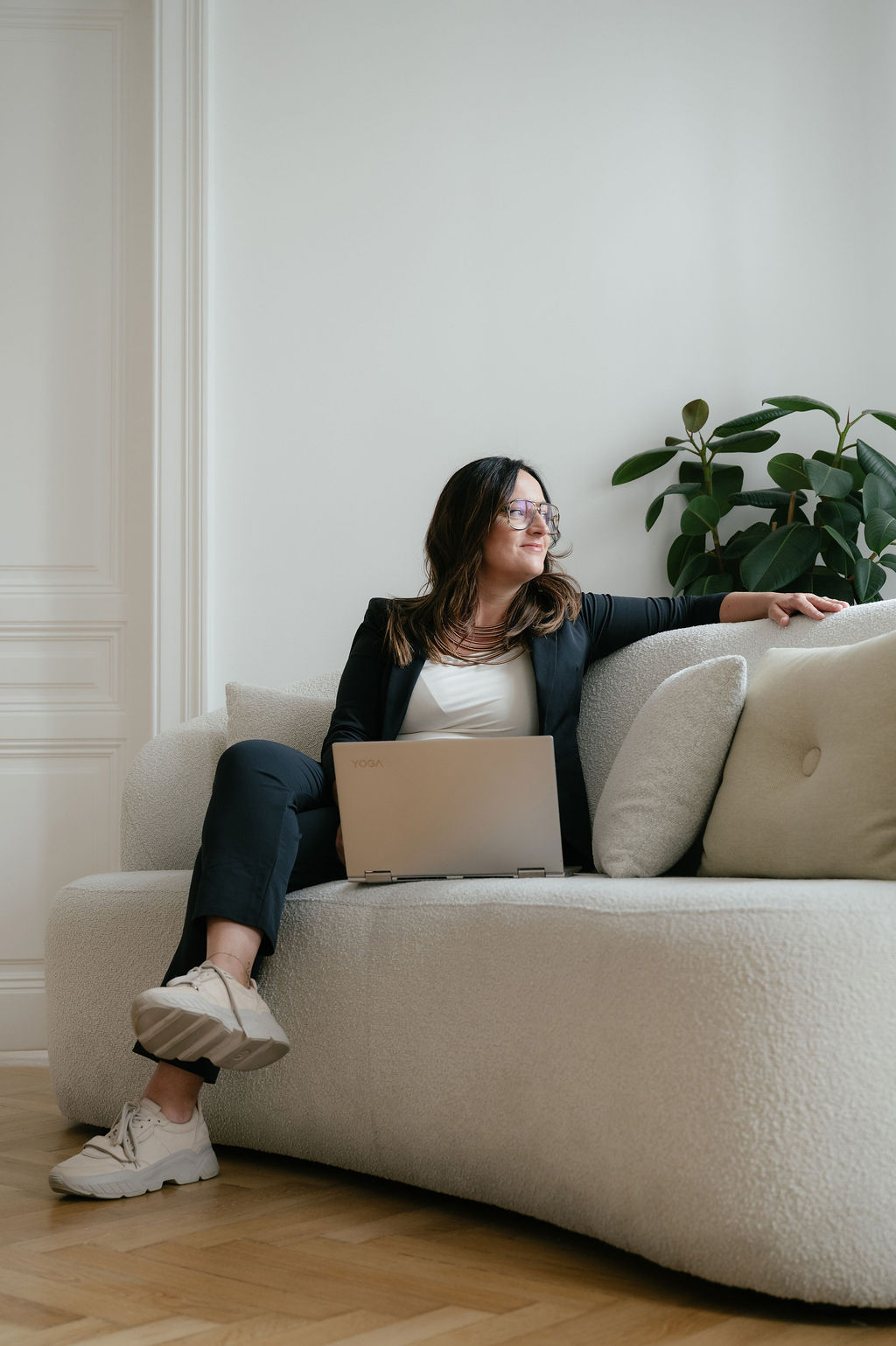 Daniela Reisner, Business-Coach in schwarzem Kostüm sitzend mit Laptop auf einer beigen Couch, dahinter eine grüne Pflanze.