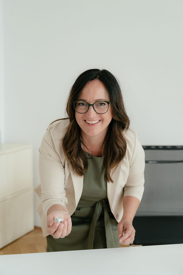 Daniela Reisner, in die Kamera blickend mit Würfel in der Hand. Daniela ist Coach für klare Auftritte.