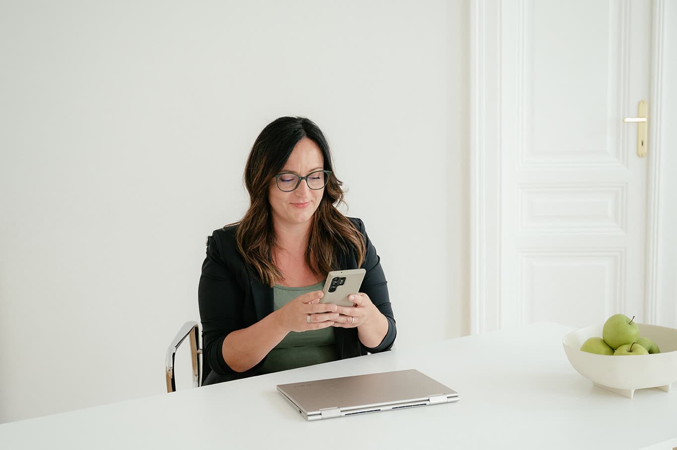Daniela Reisner mit Handy und Laptop am Schreibtisch sitzend und arbeitend.